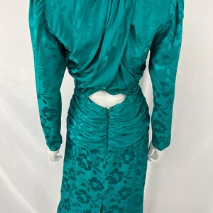 May include: Teal-colored vintage dress with a floral pattern. The dress features long sleeves, a ruched waist, and a keyhole back. The fabric has a subtle sheen, and the dress is displayed on a mannequin.