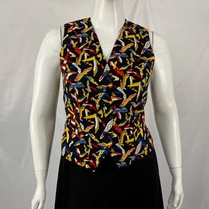 May include: A black vest with a V-neck, adorned with a colorful pattern of abstract shapes in yellow, red, blue, and white. The vest is sleeveless and appears to be made of a lightweight fabric.
