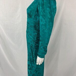 May include: A teal green dress with long sleeves and a floral pattern. The dress has a ruched waist and a V-neckline. The dress is displayed on a mannequin.