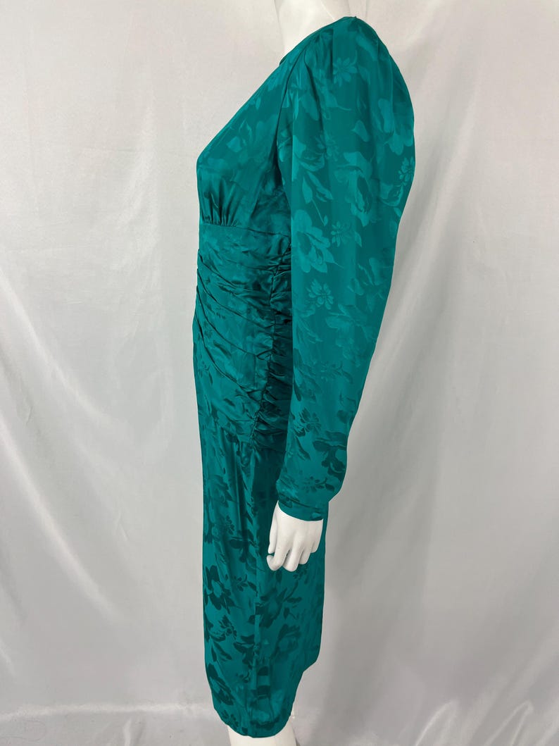 May include: A teal green dress with long sleeves and a floral pattern. The dress has a ruched waist and a V-neckline. The dress is displayed on a mannequin.