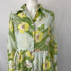 May include: A vintage dress featuring a floral pattern with yellow and white flowers, green leaves, and a light blue background. The dress has a collared neckline, long sleeves, and button-down front.