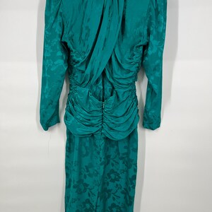 May include: Teal-colored vintage dress with long sleeves and a floral pattern. The dress features a ruched waist and a draped back detail. The fabric has a subtle sheen, adding to its elegant appearance. The dress is a midi length.