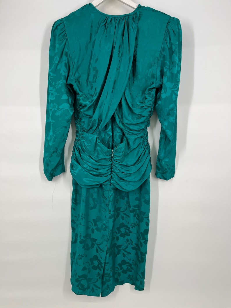 May include: Teal-colored vintage dress with long sleeves and a floral pattern. The dress features a ruched waist and a draped back detail. The fabric has a subtle sheen, adding to its elegant appearance. The dress is a midi length.