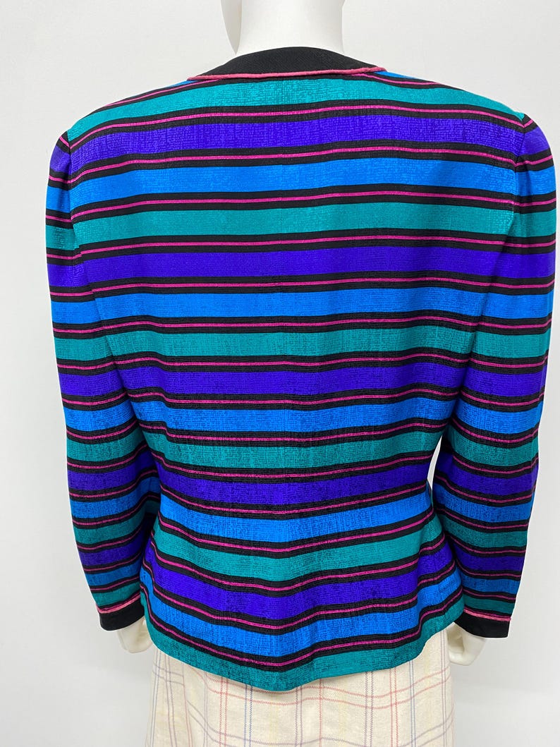 May include: A colorful, striped blazer in shades of teal, blue, purple, and pink. The long-sleeved jacket has a black collar and cuffs. The back of the blazer is shown on a mannequin.