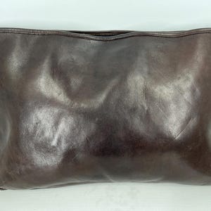 May include: A dark brown leather clutch bag with a zipper closure.