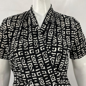 May include: Black and white patterned wrap dress. The dress features a geometric design with short sleeves and a draped neckline. The fabric has a repeating pattern of white shapes on a black background.