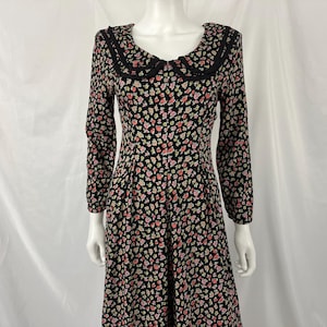 May include: A black floral print dress with a Peter Pan collar. The long-sleeved dress features a pattern of small pink and white flowers. The collar is trimmed with black lace. The dress is displayed on a mannequin.