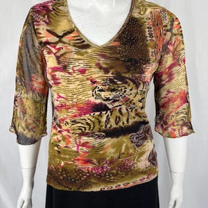 May include: A V-neck top with a colorful abstract pattern in shades of brown, olive green, pink, and orange. The top has three-quarter sleeves and is displayed on a mannequin. The fabric appears to be sheer.