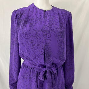 May include: A purple dress with long sleeves and a matching tie belt. The dress features a small black dot pattern and a round neckline. The dress is displayed on a mannequin.