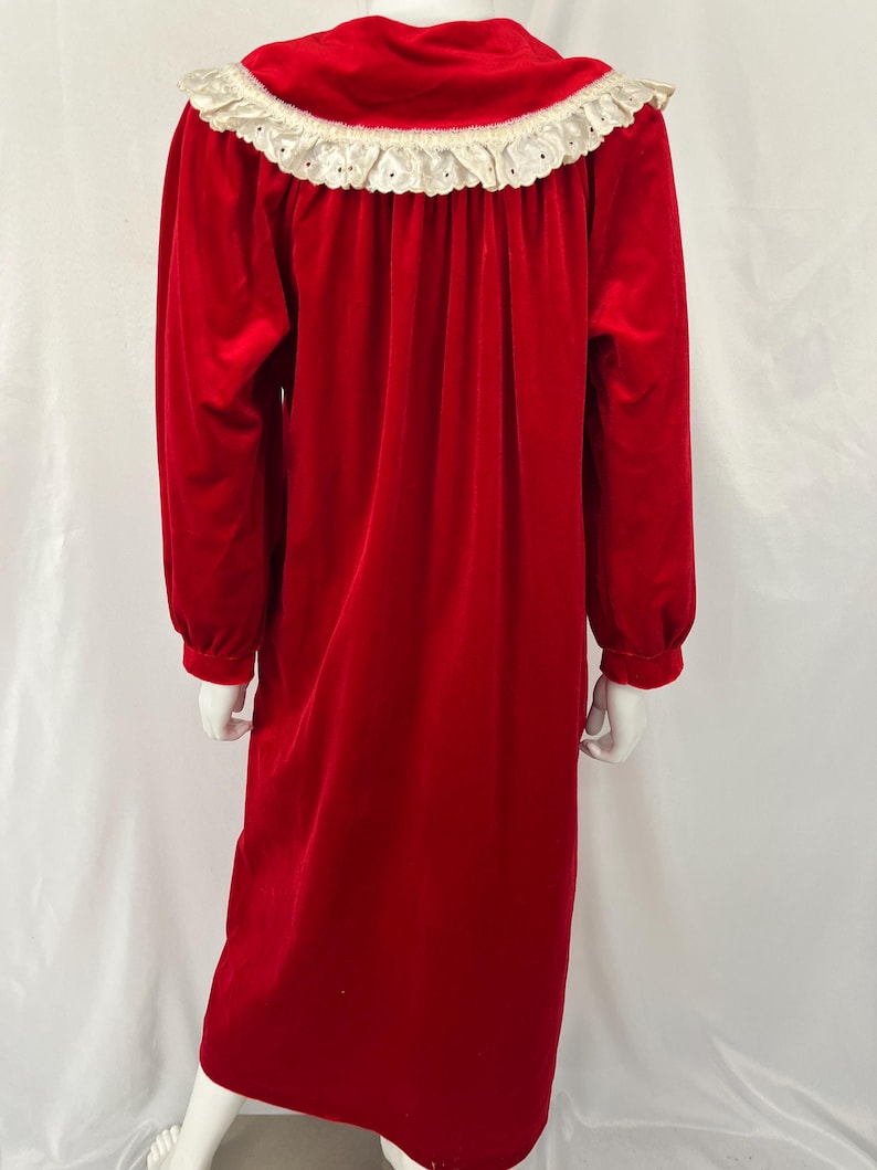 Op de afbeelding: Een lange, rode fluwelen nachtjapon met lange mouwen en een witte kanten kraag. De nachtjapon heeft een klassiek, elegant ontwerp. De kraag is afgewerkt met delicate kanten details.