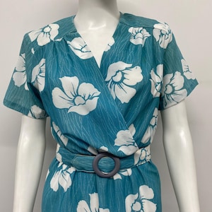 May include: A teal wrap dress with white floral patterns. The dress features short sleeves, a matching belt with a gray buckle, and a V-neckline. The fabric has a subtle textured pattern.