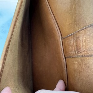 May include: Open view of a brown leather bag's interior. The bag's interior is a lighter shade of brown than the exterior. The stitching is visible along the seams. The bag appears to be well-worn.