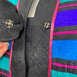 May include: Close-up of a vintage jacket with a black textured lapel and a colorful striped pattern. The stripes include teal, blue, purple, and pink. The jacket has a black button closure.