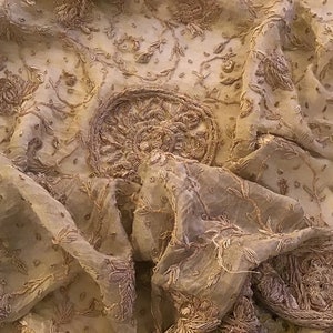 Peut inclure: Un tissu transparent avec des broderies dorées complexes. Le tissu est drapé et plié, mettant en valeur les motifs floraux délicats et un motif circulaire plus grand au centre.