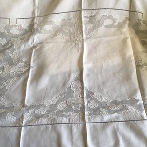 May include: White linen tablecloth with delicate embroidered designs of clouds and figures. The embroidery is intricate and detailed, creating a beautiful and elegant pattern.