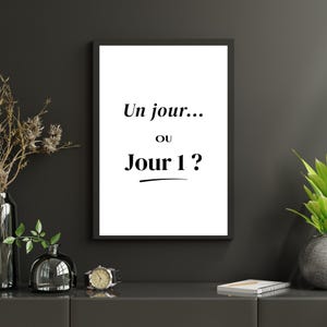 Peut inclure: Une affiche murale rectangulaire dans un cadre noir présentant un fond blanc avec le texte noir Un jour... ou Jour 1 ? La typographie est centrée avec une ligne horizontale sous le mot Jour 1, créant un affichage visuel épuré et sobre.