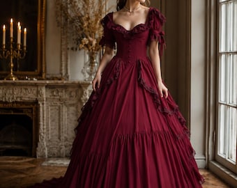 May include: A floor-length deep burgundy gown featuring a sweetheart neckline, short puffed sleeves with ribbon ties, a fitted bodice with a central row of buttons, and a voluminous skirt accented with tiered lace trim along the edges.