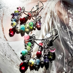 Op de afbeelding: Handgemaakte oorbellen met een zilveren draadontwerp. De oorbellen zijn versierd met kleurrijke kralen in verschillende vormen en maten, waaronder rood, roze, groen en blauw. Een uniek en opvallend accessoire met een haaksluiting.