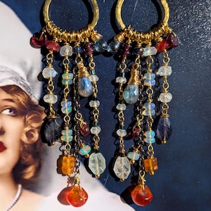 Puede incluir: Un par de pendientes de aro dorados con un diseño en cascada de cuentas de piedras preciosas multicolores. Los pendientes incluyen varias piedras facetadas en tonos naranja, azul, transparente y rojo oscuro, suspendidas de aros y cadenas.