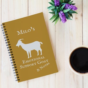 May include: A gold spiral bound notebook with the text "Milo's Emotional Support Goat & Notes" and a white silhouette of a goat on the cover.