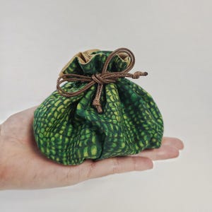 Peut inclure: Un petit sac à cordon vert avec un cordon brun et un motif vert et brun. Le sac est en tissu et a une surface texturée.