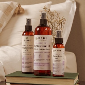 May include: Three amber plastic spray bottles of Bare Botanics Unscented Magnesium Oil with white labels. The center bottle is 16oz, while the two flanking bottles are 8oz. Each label features black text, a leaf icon, and details about the product.