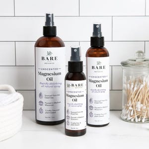 May include: Three brown glass spray bottles of unscented magnesium oil. The bottles are labeled "BARE BOTANICS -UNSCENTED- Magnesium Oil" and feature a leaf design. The bottles are on a white tiled surface.