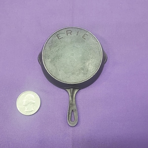 May include: A small cast iron skillet with a black handle. The skillet has the word "ERIE" embossed on the side.