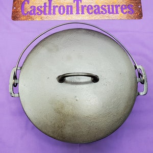 May include: A black cast iron Dutch oven with a lid and a handle. The lid has a metal ring handle. The oven is on a purple surface.