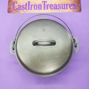 May include: A black cast iron Dutch oven with a lid and a handle. The lid has a number "8" embossed on it. The oven is on a purple background.