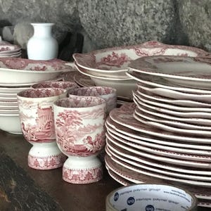 Puede incluir: Una colección de platos de porcelana vintage con estampado rosa y blanco, que incluye platos, cuencos y hueveras. Los platos están dispuestos sobre una superficie de madera.