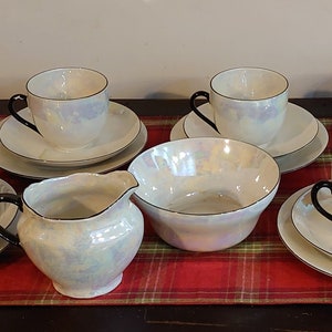 Può includere: Un set di tazze da tè e piattini bianchi con finitura madreperlacea e bordo nero. Il set comprende una brocca per la panna e una zuccheriera.