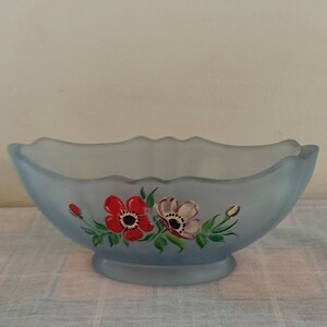 May include: A frosted blue glass bowl with a scalloped rim and painted floral design. The flowers are red, white, and green.
