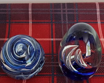 May include: Two glass paperweights with blue and white swirling patterns. The paperweights are on a red and black checked surface.