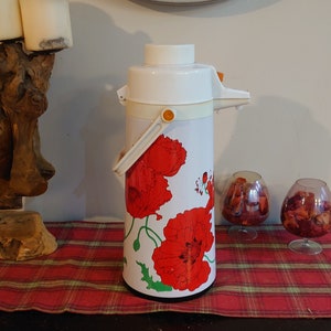 Puede incluir: Cafetera térmica blanca con un diseño floral de amapolas rojas. La cafetera tiene una tapa blanca y un asa.