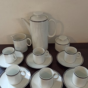 May include: A white porcelain coffee set with black trim. The set includes a coffee pot, creamer, sugar bowl, and six cups and saucers.