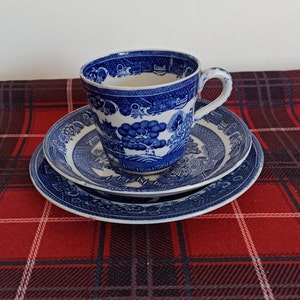 May include: A blue and white teacup and saucer set with a floral pattern. The set is on a red and black checked tablecloth.