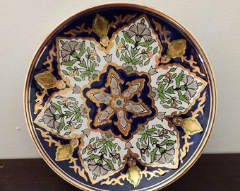 May include: A decorative ceramic plate with a blue and white floral design. The plate has a gold rim and intricate details.
