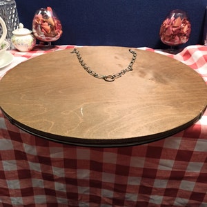 May include: A round wooden mirror with a metal chain hanging from the top. The mirror is sitting on a red and white checkered tablecloth.