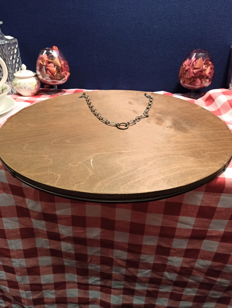 May include: A round wooden mirror with a metal chain hanging from the top. The mirror is sitting on a red and white checkered tablecloth.