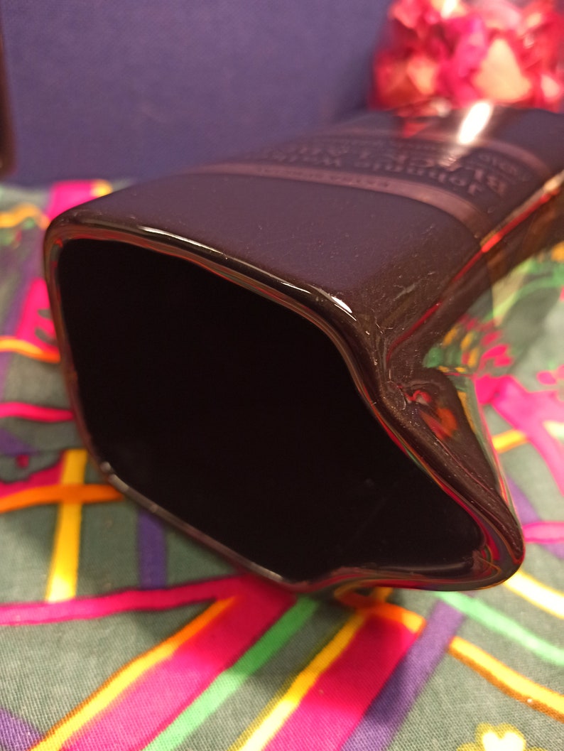 May include: A black ceramic pitcher with a glossy finish. The pitcher has a wide opening and a rounded shape. The pitcher is sitting on a colorful fabric with a plaid pattern.