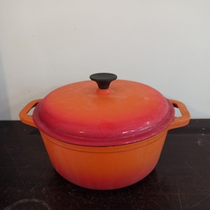 Op de afbeelding: Oranje en rode geëmailleerde gietijzeren stoofpot met een zwarte knop op de deksel.