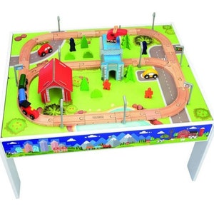 Puede incluir: Una mesa de tren de madera con una superficie de juego verde y azul. La mesa cuenta con una vía de tren, un edificio rojo, una torre azul y una variedad de otros accesorios. La mesa es blanca y tiene cuatro patas.
