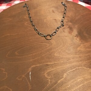May include: The back of a round wooden wall mirror with a silver chain and a brass ring for hanging.