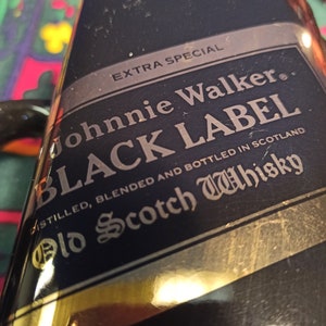 May include: A black bottle with a gold label that reads "EXTRA SPECIAL Johnnie Walker BLACK LABEL" and "DISTILLED, BLENDED AND BOTTLED IN SCOTLAND Old Scotch Whisky".