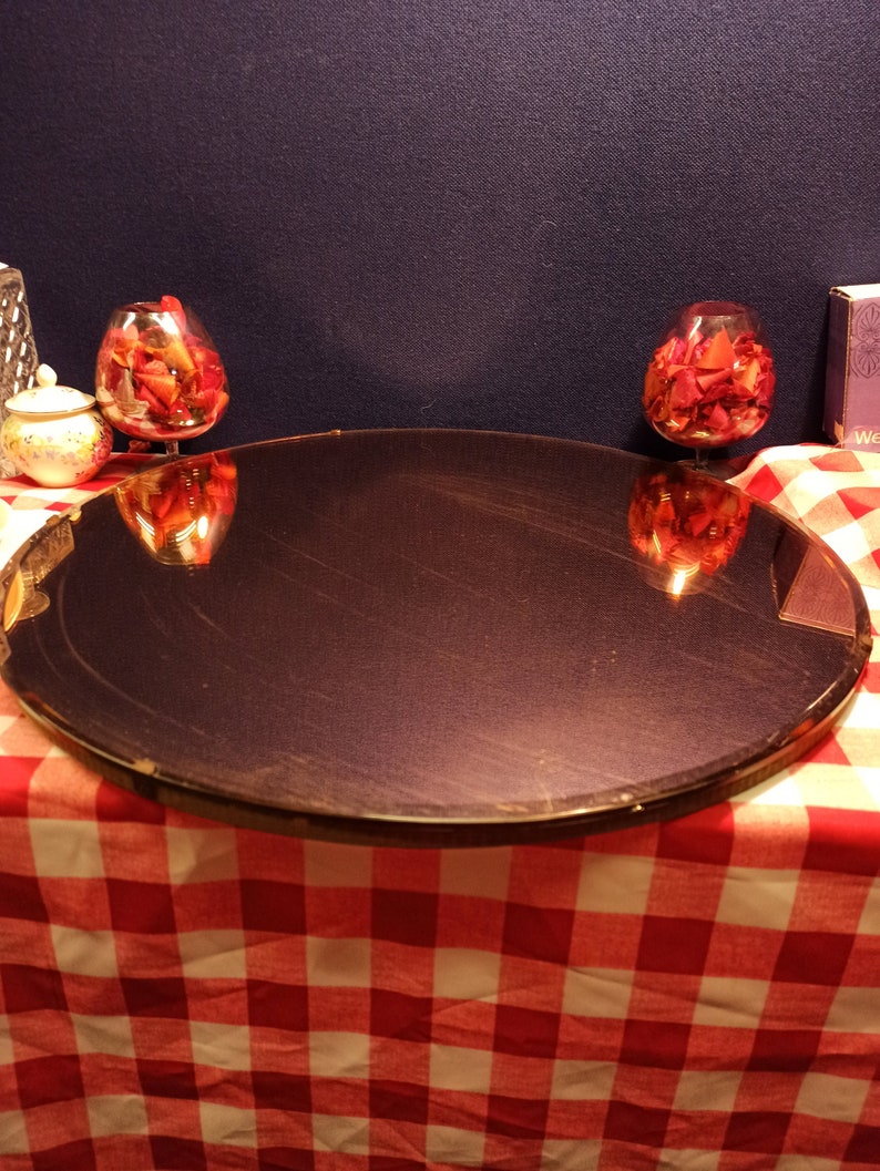 May include: A round, dark brown, mirrored tray with a gold rim sits on a red and white checkered tablecloth. Two clear glass bowls filled with red rose petals are reflected in the tray.