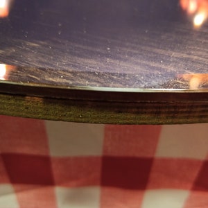 May include: Close-up of a dark purple round table top with a wooden edge. The table top is covered in a fine layer of dust. The table is sitting on a red and white checkered tablecloth.