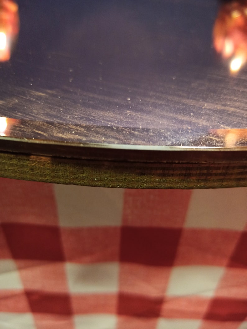May include: Close-up of a dark purple round table top with a wooden edge. The table top is covered in a fine layer of dust. The table is sitting on a red and white checkered tablecloth.