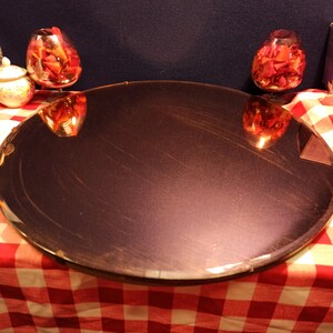 May include: A round, dark purple mirror sits on a red and white checkered tablecloth. Two glass bowls filled with red rose petals are reflected in the mirror.