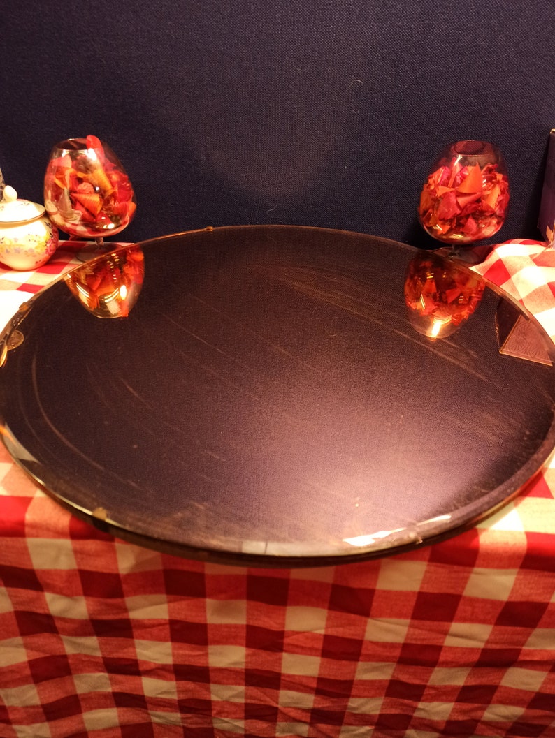 May include: A round, dark purple mirror sits on a red and white checkered tablecloth. Two glass bowls filled with red rose petals are reflected in the mirror.